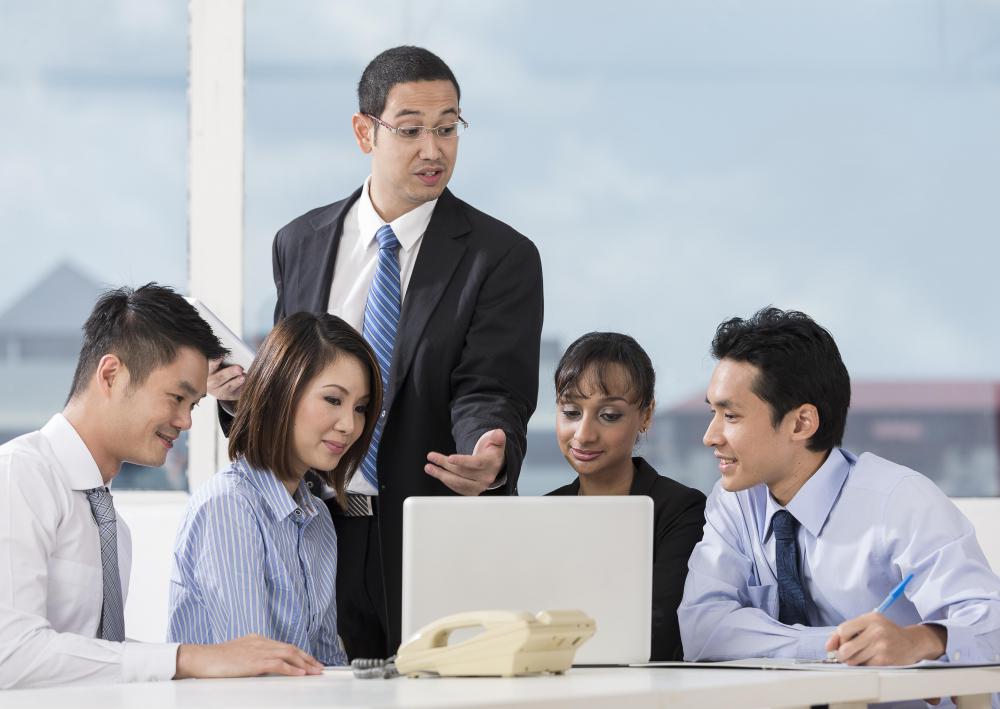 man-standing-in-suit-near-four-business-people-looking-at-computer